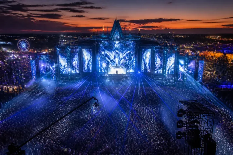 aerial twilight view of a huge festival mainstage with lasers and a packed crowd in front of a silhouetted dj