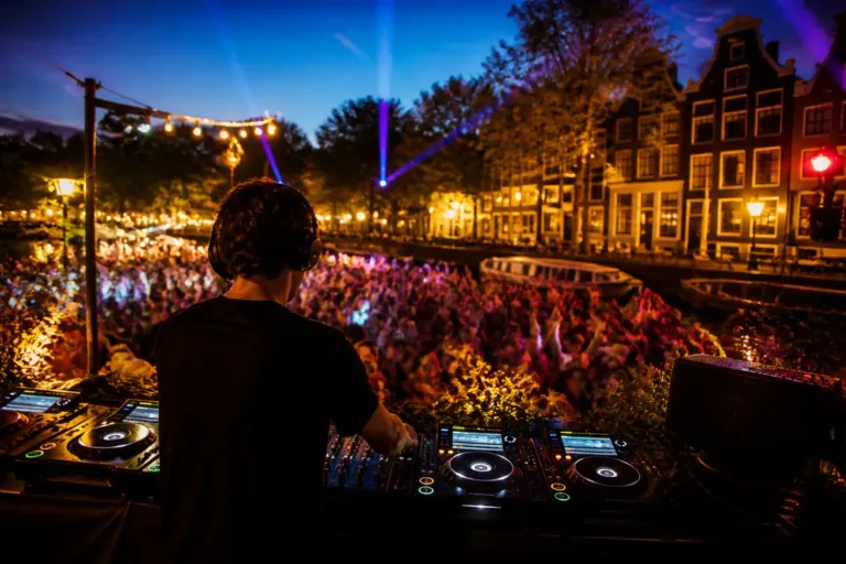 dj on an outdoor festival stage at dusk playing for a dense, cheering crowd