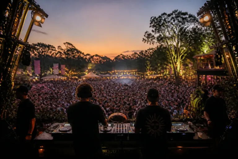 open-air festival dj booth seen from behind with duo, crowd, staff and surrounding food stalls